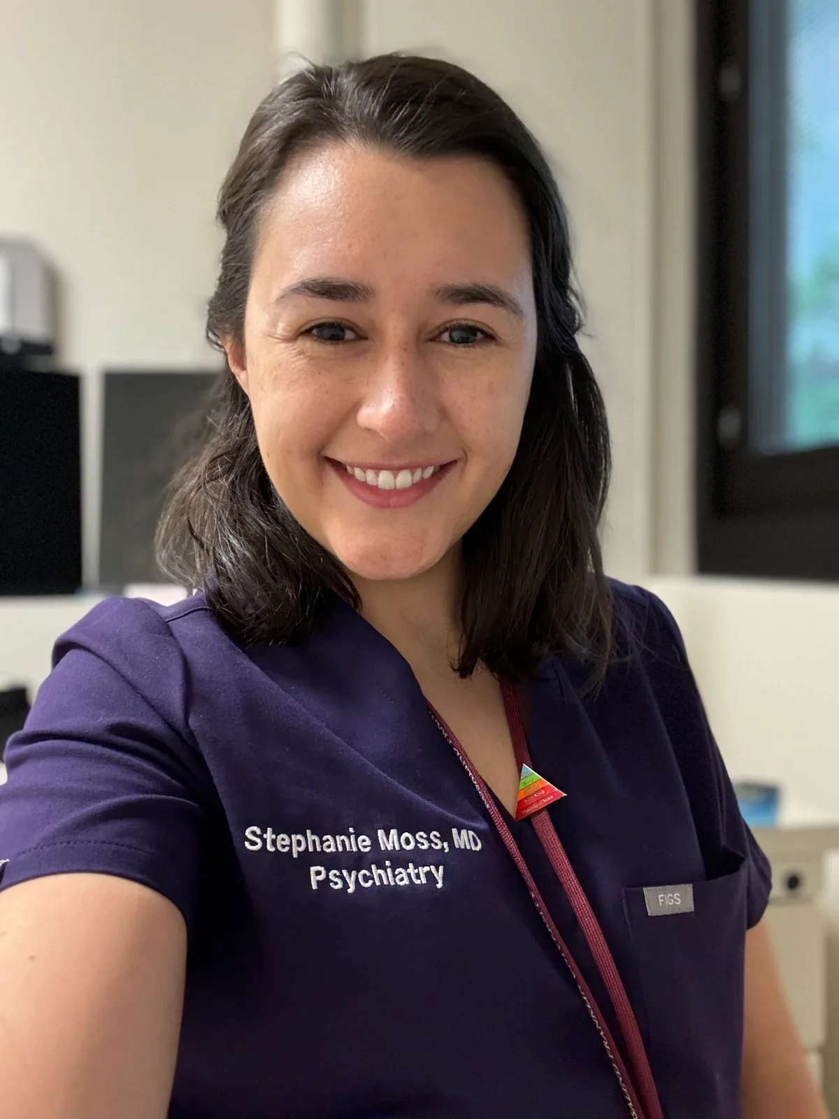 Stephanie Moss, MD, smiling in navy scrubs embroidered Stephanie Moss, MD Psychiatry.